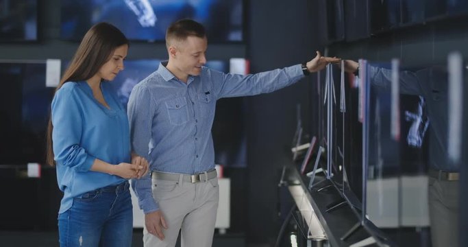 Couple in shopping. They are looking for new tv. They are pointing fingers at tv. Shallow depth of field. 4K UHD