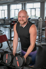 Fototapeta na wymiar handsome young man in blue shorts and black t-shirts, doing exercises for biceps in the gym. bald man smiling at camera