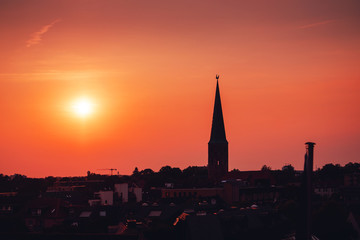 Fototapeta na wymiar Beautiful and colorful summer sunset roof top view of a old historic church tower above the city. Warm red and orange sky color tones. Old town of Braunschweig, Germany