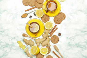 Ginger tea in a cup with ginger roots and lemon on marble textured background, top view. A healthy lifestyle, anti-flu and anti-inflammatory concept.