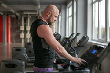 Fototapeta na wymiar Fit Muscle bald Man With Headphones Running on Treadmill in Gym.