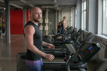 Fototapeta premium Fit Muscle bald Man With Headphones Running on Treadmill in Gym.