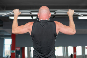 Athlete muscular fitness bald man  pulling up on horizontal bar in a gym Close-up