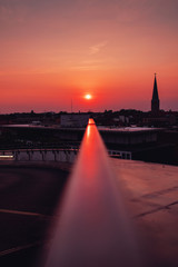 Obraz premium Urban Park deck rooftop view with Glass structure and church on the horizon with sunset light reflection on the metal. Colorful warm summer light view. Old town of Braunschweig, Germany