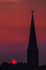 Fototapeta premium Beautiful and colorful summer sunset roof top view of a old historic church tower above the city. Warm red and orange sky color tones. Old town of Braunschweig, Germany