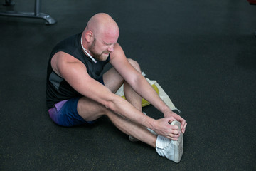 Naklejka premium bald man in black t-shirt having pain in leg after exercise in the gym.