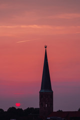 Fototapeta premium Beautiful and colorful summer sunset roof top view of a old historic church tower above the city. Warm red and orange sky color tones. Old town of Braunschweig, Germany
