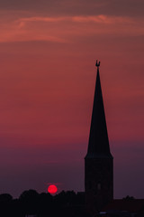Fototapeta premium Beautiful and colorful summer sunset roof top view of a old historic church tower above the city. Warm red and orange sky color tones. Old town of Braunschweig, Germany