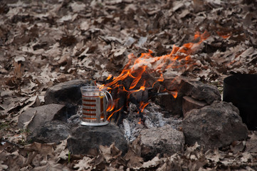 Glass of tea in the cup holder by the burning fire at a picnic in the oak forest