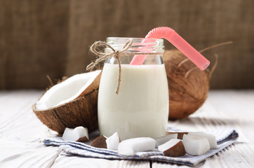 Mason jar of milk or yogurt on blue napkin on white wooden table with coconut aside