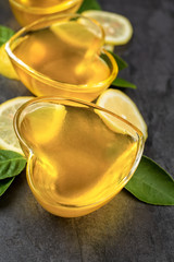 Yellow lemon jelly in heart shaped glass with cut lemon slices on dark background, vertical composition, top view