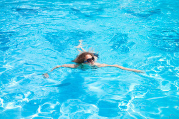 The girl swims in the pool on a hot summer day at the resort.