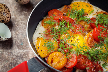 Fried quell eggs with tomato’s and dill on frying pan, close up.