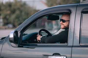  Bald and bearded man in glasses with a clock in a suit behind the wheel of a  black car. motorists concept