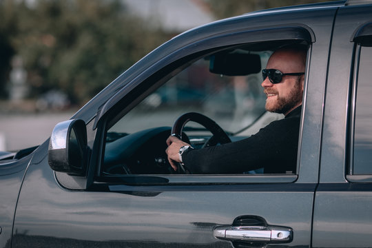  Bald and bearded man in glasses with a clock in a suit behind the wheel of a  black car. motorists concept