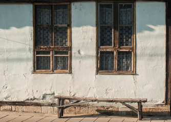Fototapeta na wymiar Old country house facade with weathered wooden windows and bench in sunny day