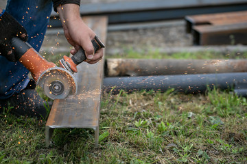 a Canadian man in blue jeans and black boots is sawing a metal profile with a Bulgarian sparks are flying