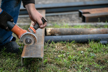 a man in blue jeans and black boots is sawing a metal profile with a Bulgarian sparks are flying