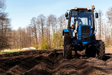 Blue tactor plows field in spring. Male farmer working in field.