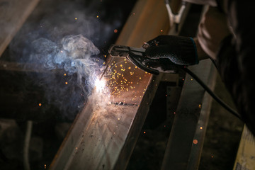 Close up of a male welder in uniform  and welders leather weld metal with an arc welding machine at...