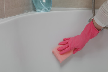 Housemaid in the rubber gloves cleaning bathroom with a sponge