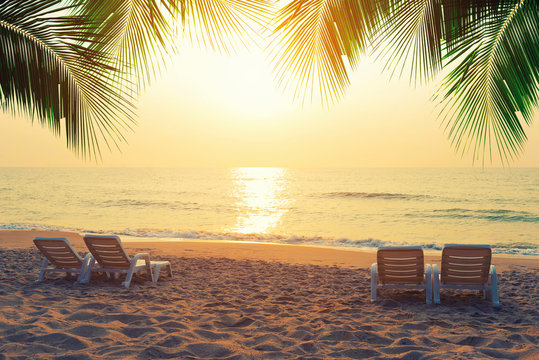 Beach chairs with coconut leaves on the tropical beach at sunset. Summer travel concept. © tawanlubfah