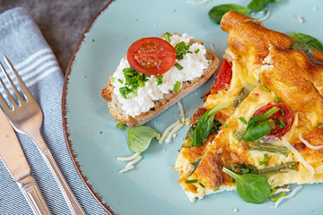 The Breakfast On Sunday Morning. Sliced pieces of omelet with bread on a plate. Omelet in the oven with green beans, tomatoes, herbs and cheese.