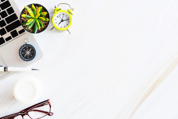 Flat lay photo in top view of business accessories, mobile, alarm clock, laptop, coffee, glasses and compass on white marble table with free copy space for text. Business and technology concept.