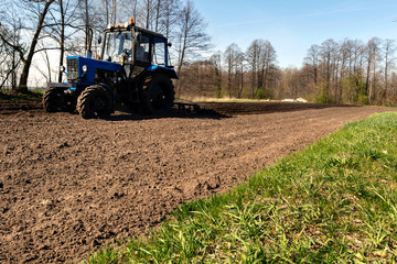 Fototapeta premium Blue tactor plows field in spring. Male farmer working in field.