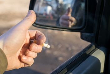 Fototapeta na wymiar closeup of male hand with the missing finger holding a cigarette in a car in a residential area