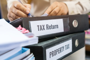 Tax return and property tax folders stack with label black binder on paperwork documents summary report in busy offices by manager checking. HR-human resources business bookkeeping accountancy Concept
