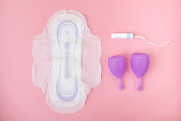Purple menstrual cup, tampon and Sanitary napkin are on a pastel pink background. The minimalist image is suitable for topics of women's health, hygiene, gynecology. Top view.