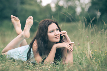 attractive young woman talking on smartphone while lying on grass on summer day. people and technology