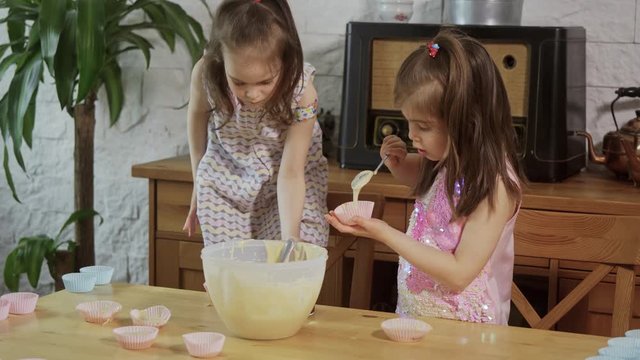 two little adorable girls put cream on the molds to make cupcakes
