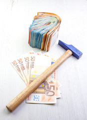 MONEY IN CASH WITH WORK HAMMER ON WOODEN TABLE