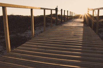 Wooden fence and walkway to beach faded. Scenic sunset on seashore. Wooden columns and path with evening sun. Travel and tourism. Empty path in sunlight. Walking concept. Camino de Santiago way.