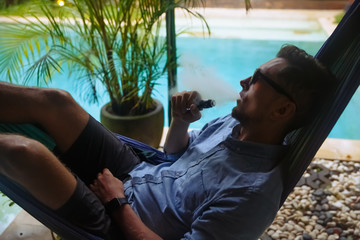 Man resting in a hammock and vaping and letting off steam from an electronic cigarette