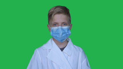 In slow motion on the background of a chromakey a young guy (boy) in a doctor's uniform in a mask. Concept of: Green background, Chromekey, Young doctor, Fashionable, Blond, Doctor.