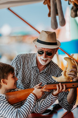 Grandfather and grandson having fun and spending good quality time together in amusement park. Kid shooting with air gun while grandpa helps him to win the prize.