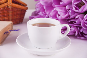 A cup of tea, book and violet tulips on the table