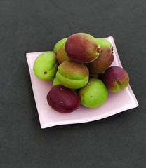 Unripe sour apricots on black ground,