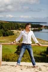 stylish guy in a white shirt is standing in the sand against the background of Nida