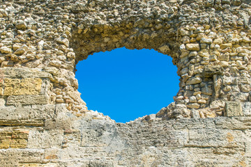 A hole in the stone wall and the blue sky in the background, a ruined wall with a hole. The image can be used as a background