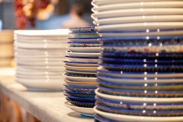 Closeup stack white and colored blue porcelain plates with oriental and ethnic ornament stands in open kitchen of trendy restaurant. Concept washing dishes, preparing for lunch, evening service