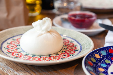 Closeup fresh local Italian soft round buratta on round color beautiful plate with a pattern served on the restaurant table. Concept mozzarella, cheese made from buffalo milk