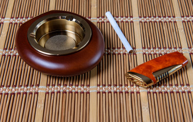Stylish exquisite ashtray with a cigarette and lighters on the table in the bar on a bamboo napkin.