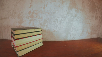 A small stack of multicolored books on a bright old brown table. Background old concrete wall.