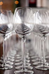 Many transparent crystal wine glasses stand in row on the brown wooden shelves of the rack. Side view. Concept of tasting, banquet, catering, buffet, lunch, anniversary, wedding, birthday