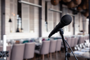 Closeup black iron microphone stands on stage background of restaurant hall served for banquet. Concept live music concert in bar evening, catering, buffet, anniversary, wedding, birthday