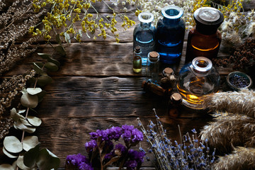 Various dried herbs and an essential oil bottles on a brown wooden board background. Herbal...